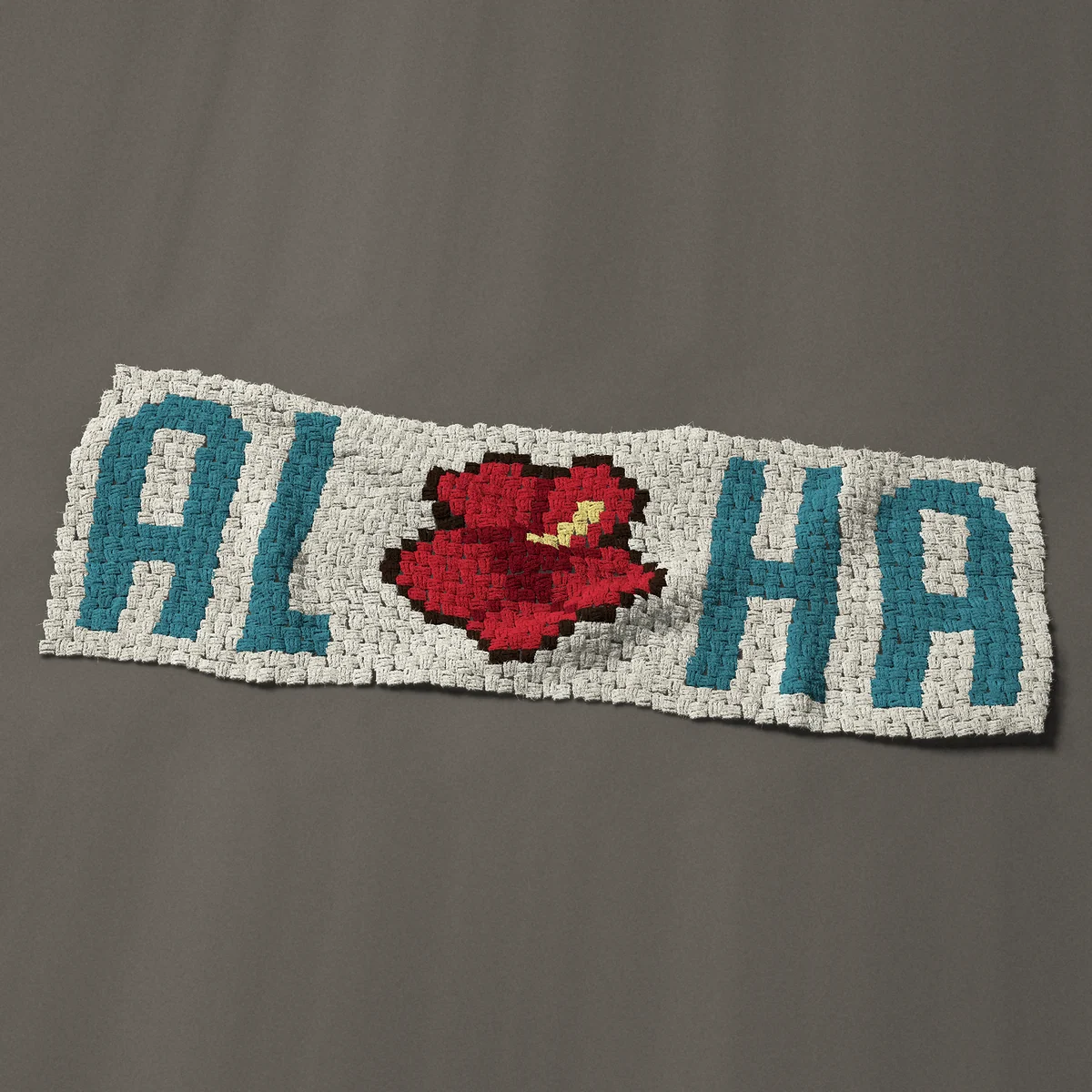 A panel worked corner to corner, 51 by 17¼ inches: Aloha in teal letters with a hibiscus flower for the O, 68 by 23 blocks