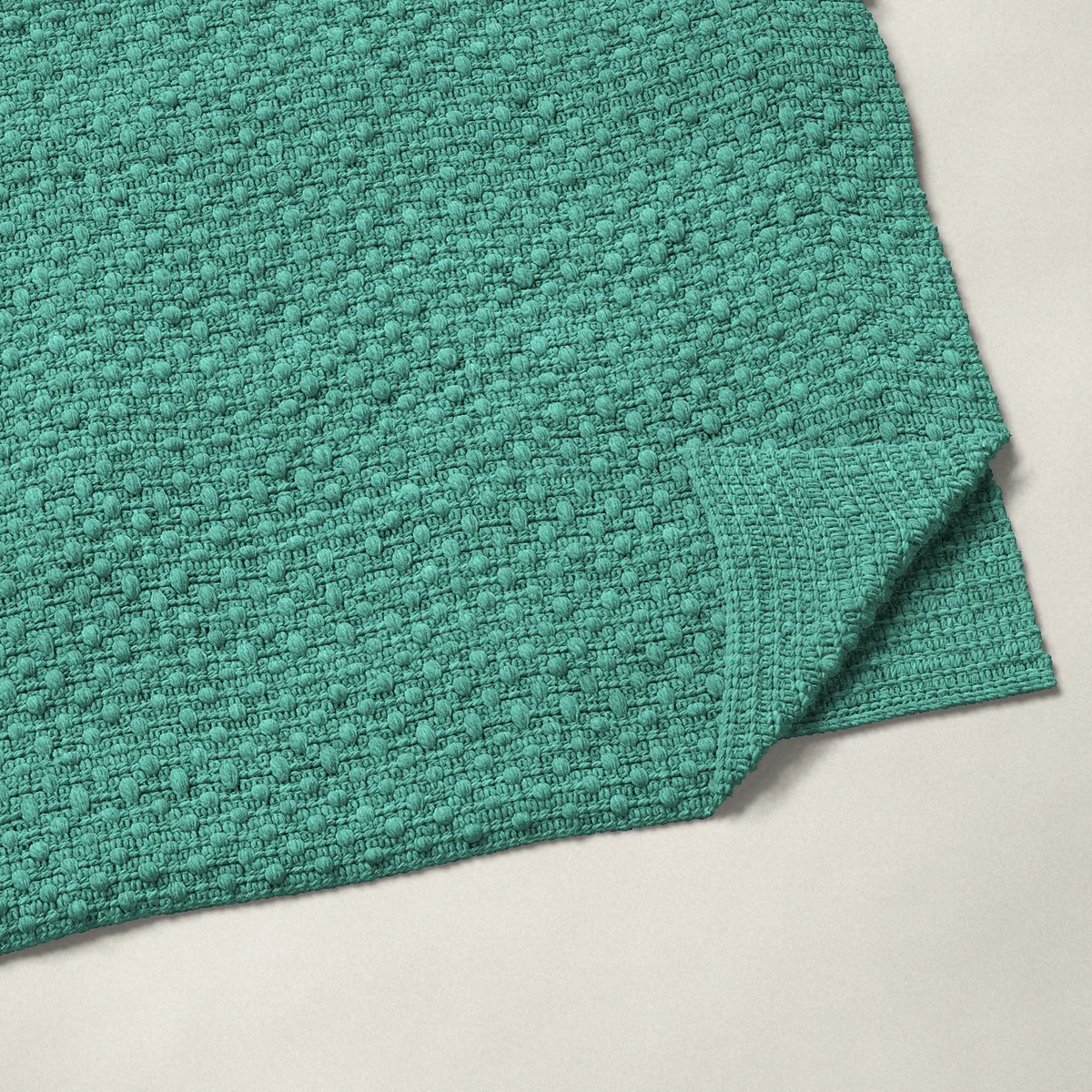 A throw in bobble stitch, 54½ by 66½ inches, folded in half with a corner turned back, showing the cloth's other side