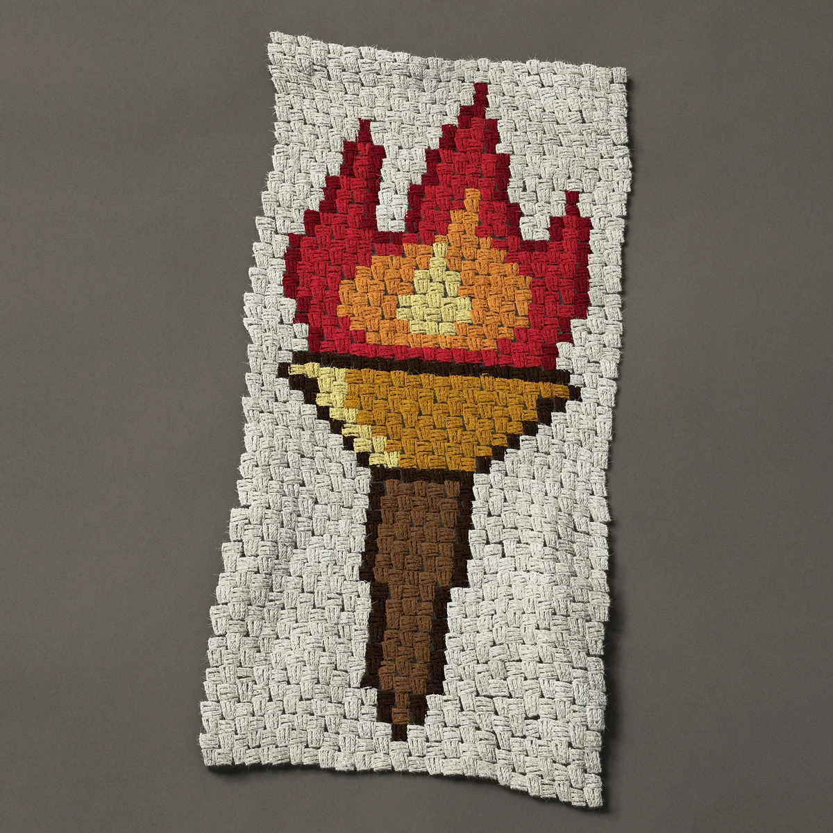 A panel worked corner to corner, 18¾ by 39½ inches: Flaming torch, fire in a gold cup on a wooden handle, 25 by 53 blocks
