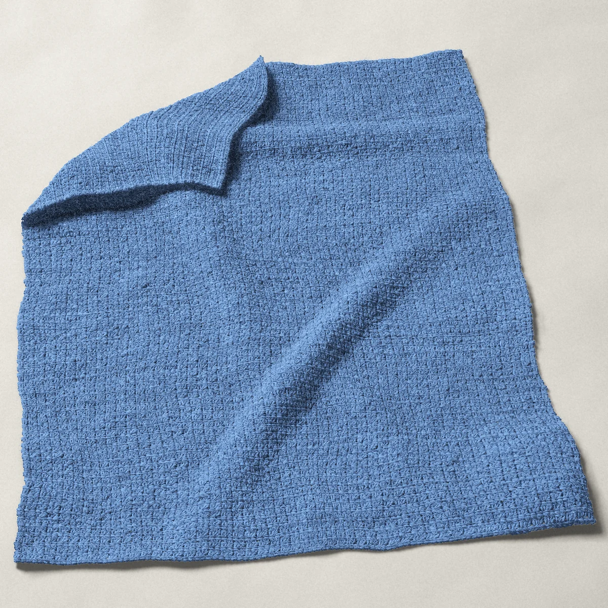 A baby blanket in grit stitch, 32 by 40 inches, spread out with a corner turned over